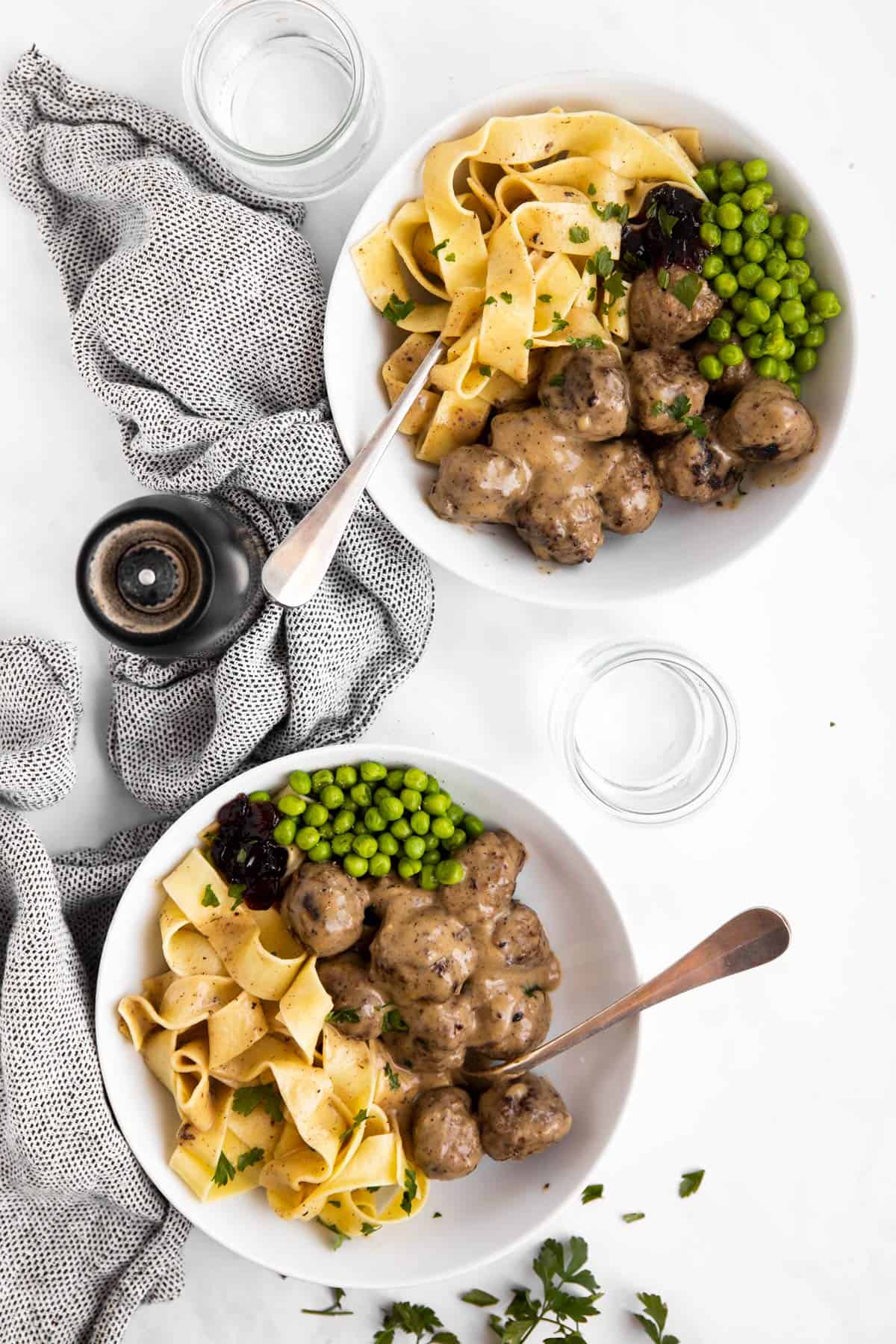 top down view of two plates with noodles, Swedish meatballs and peas