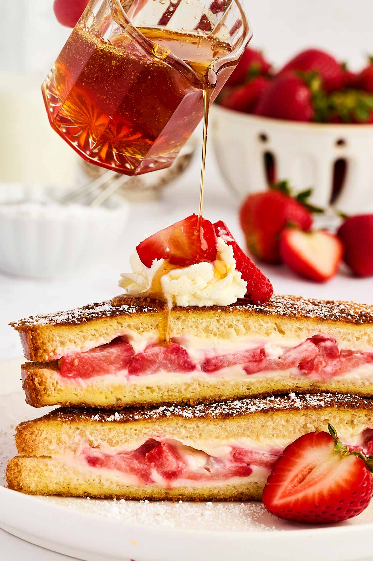 Pouring maple syrup over a stack of strawberry French toast.