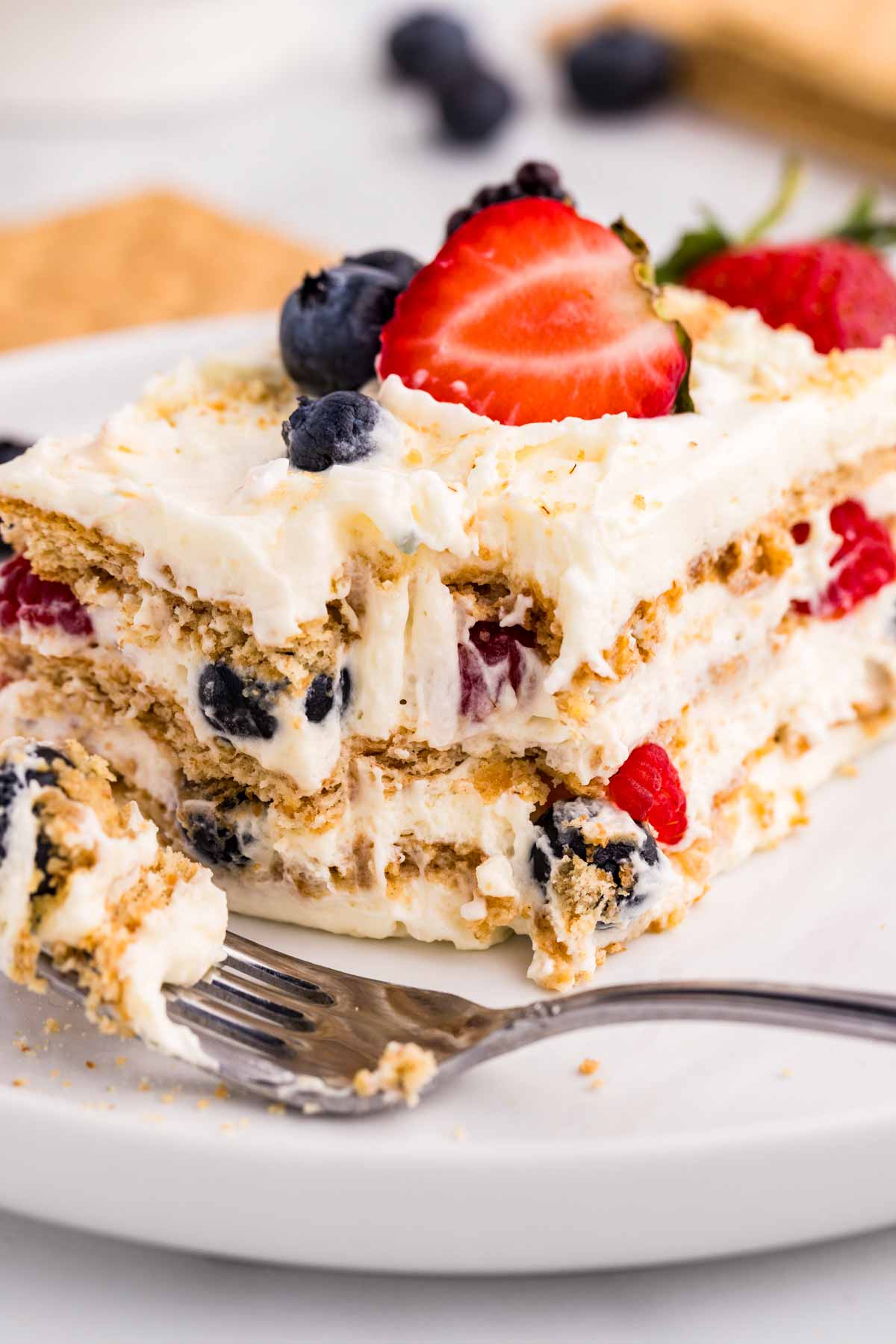 frontal closeup of berry icebox cake on plate with bite taken out