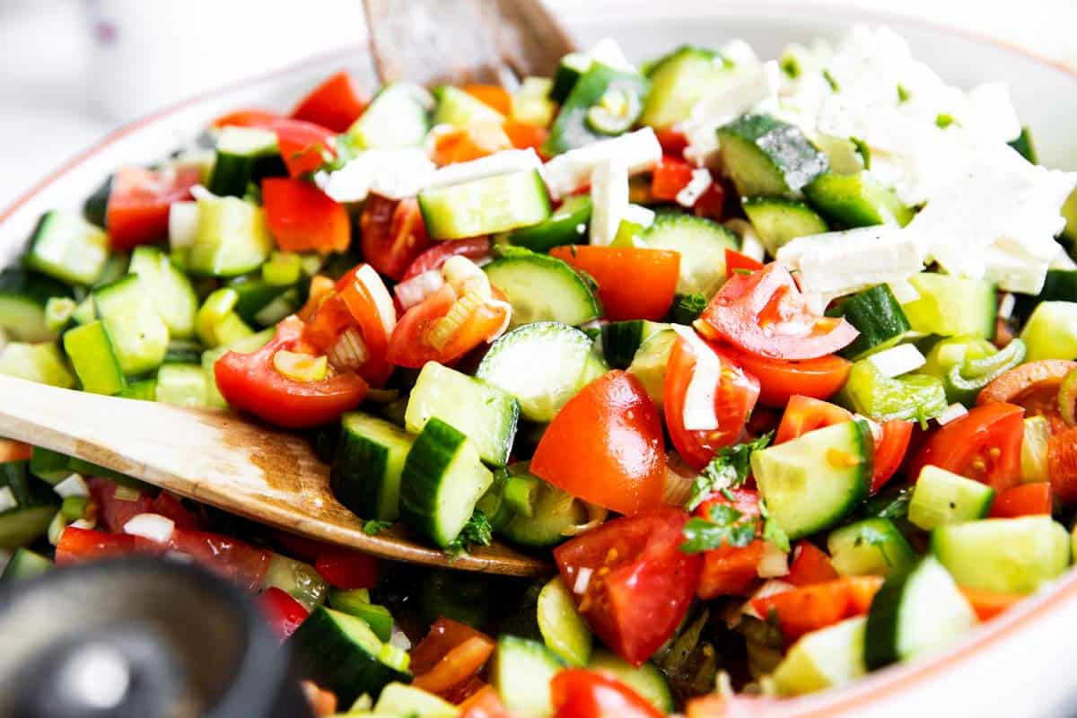 close up photo of salad tongs tossing a Shopska salad