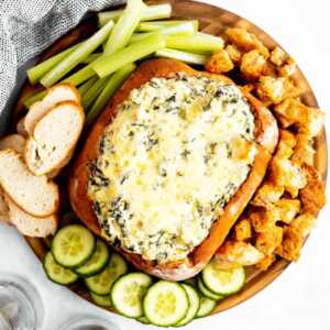 overhead view on bread bowl with spinach artichoke dip surrounded by vegetables and bread