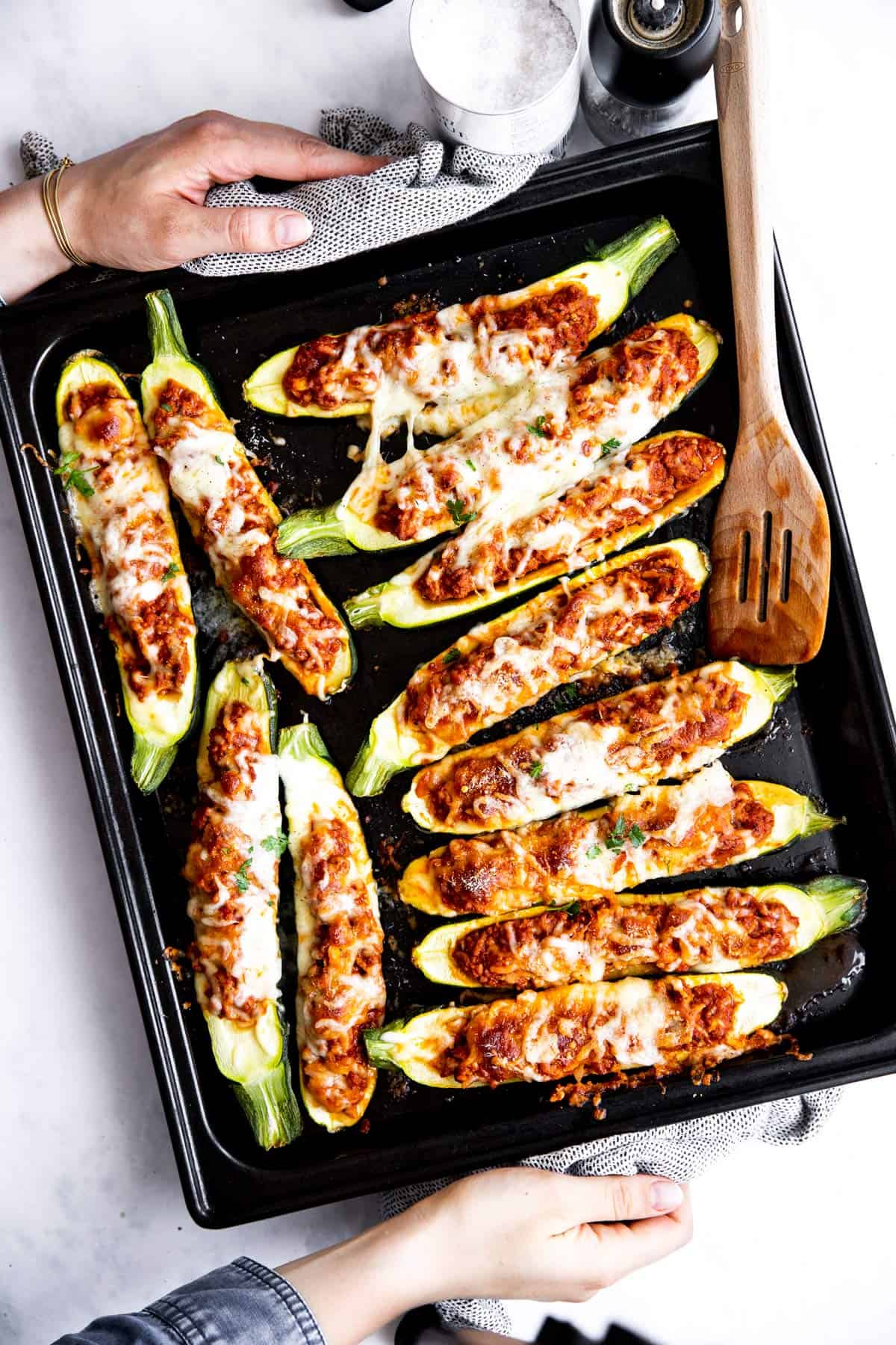 top down view of female hands holding baking sheet with stuffed zucchini