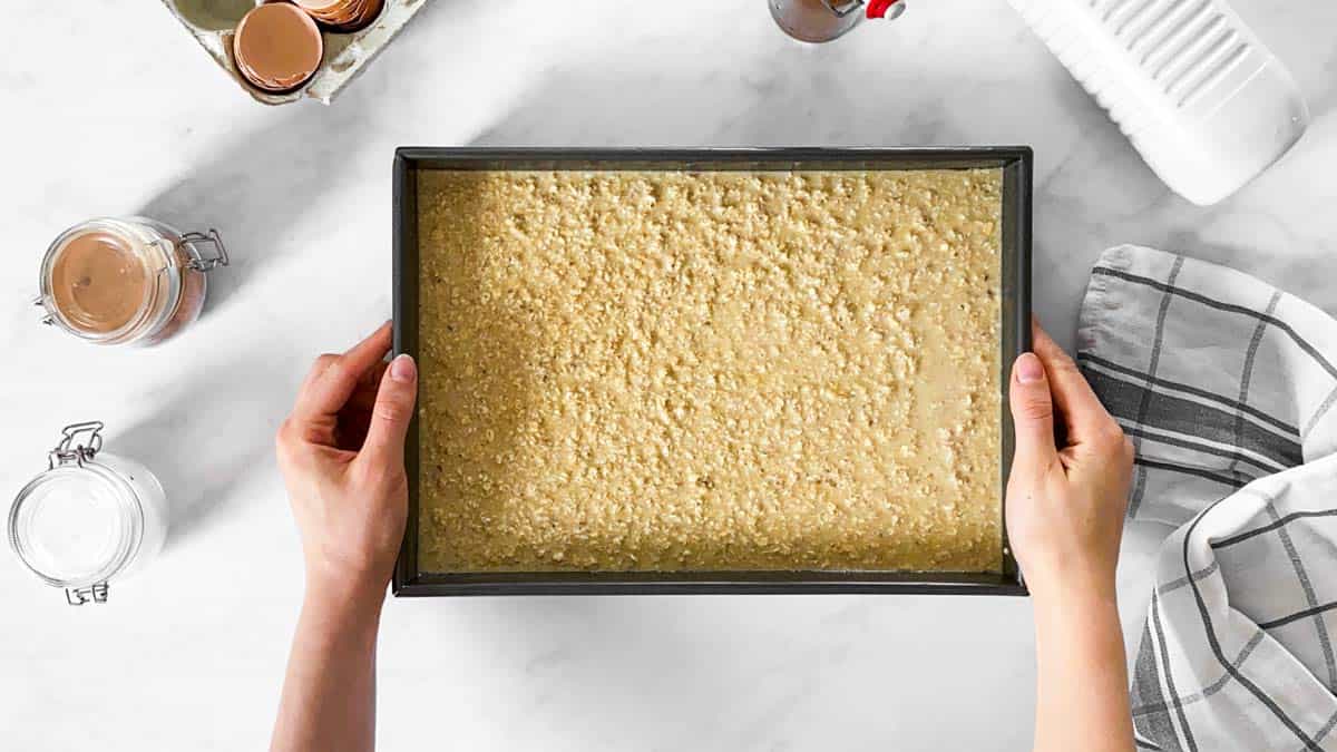 female hands holding baking pan with raw oatmeal