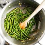 skillet with sautéed green beans and wooden spoon