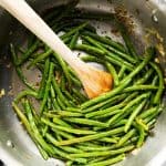 skillet with sautéed green beans and wooden spoon