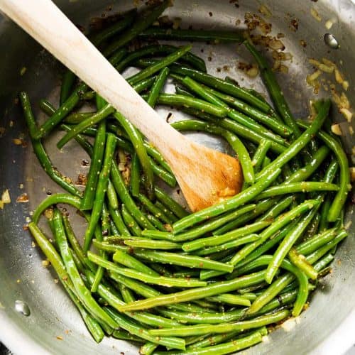 skillet with sautéed green beans and wooden spoon