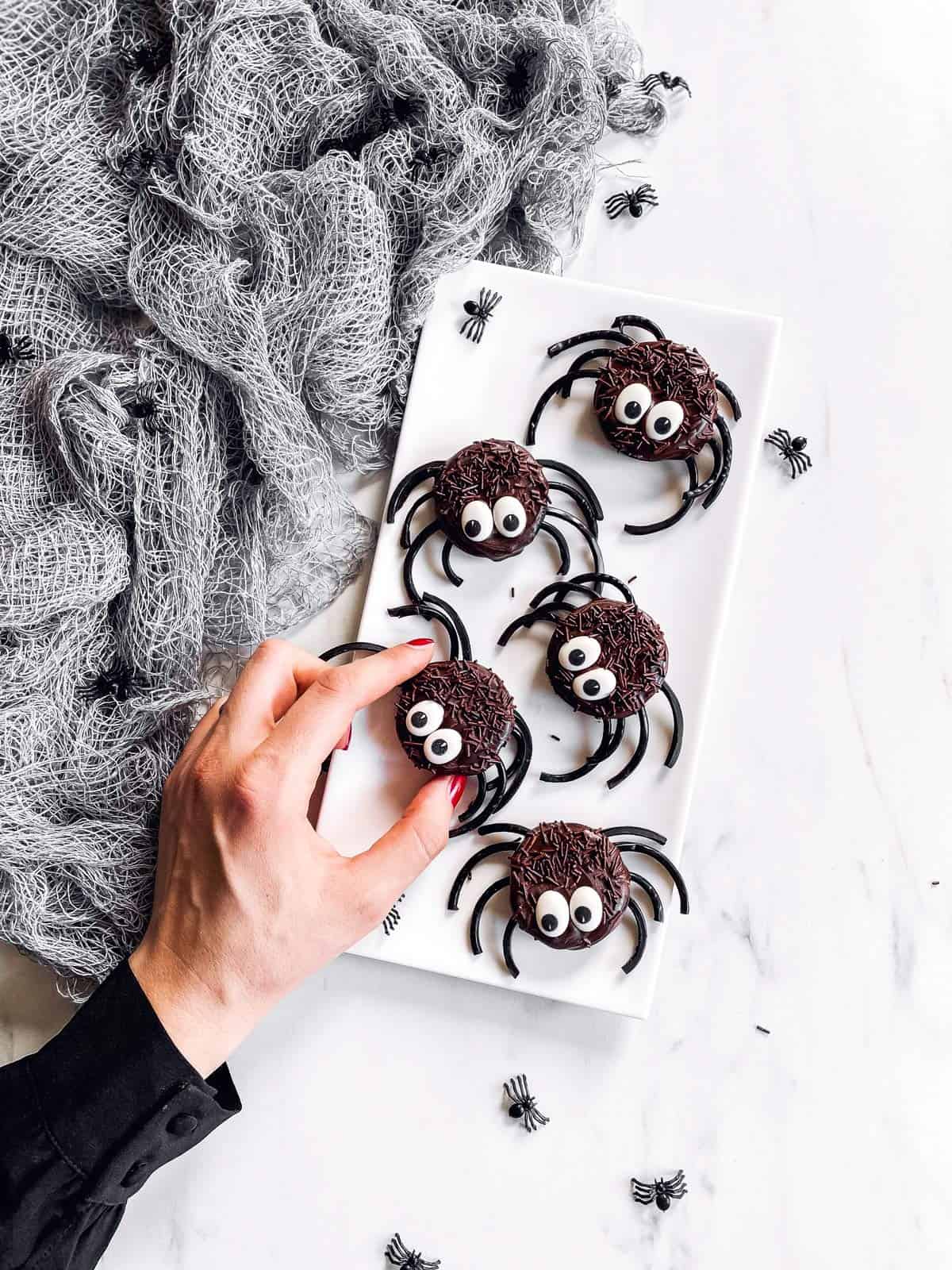 female hand taking an Oreo spider from a white platter