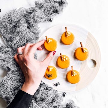 female hand grabbing a pumpkin decorated Oreo off a platter