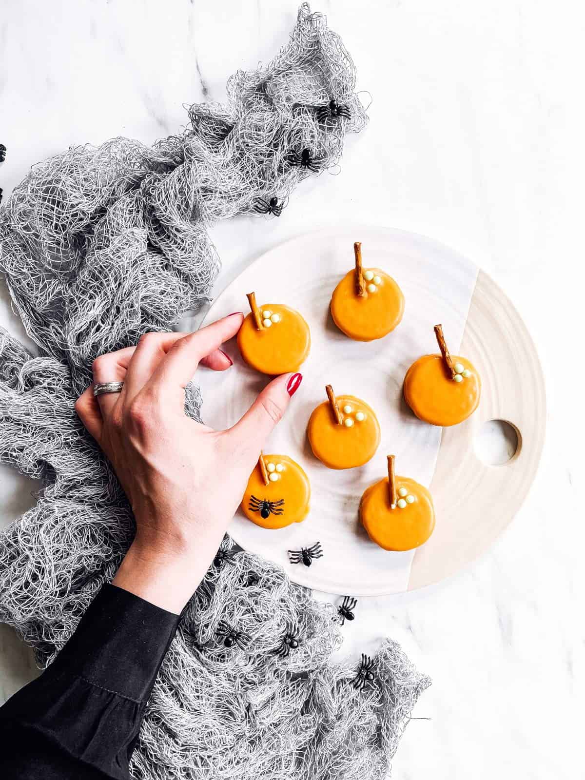 female hand grabbing a pumpkin decorated Oreo off a platter