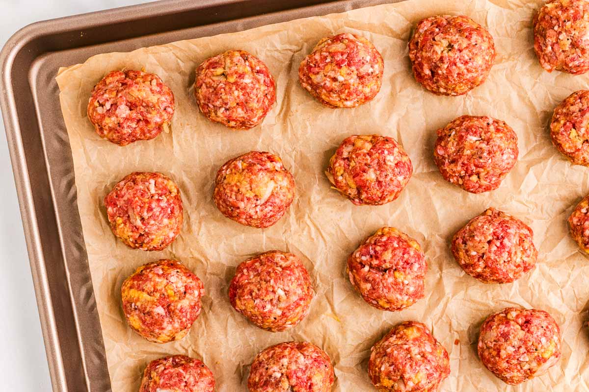 Unbaked meatballs on a lined sheet pan.