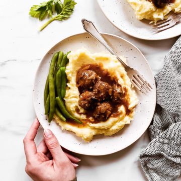 female hand holding plate with mashed potatoes, meatballs, gravy and green beans