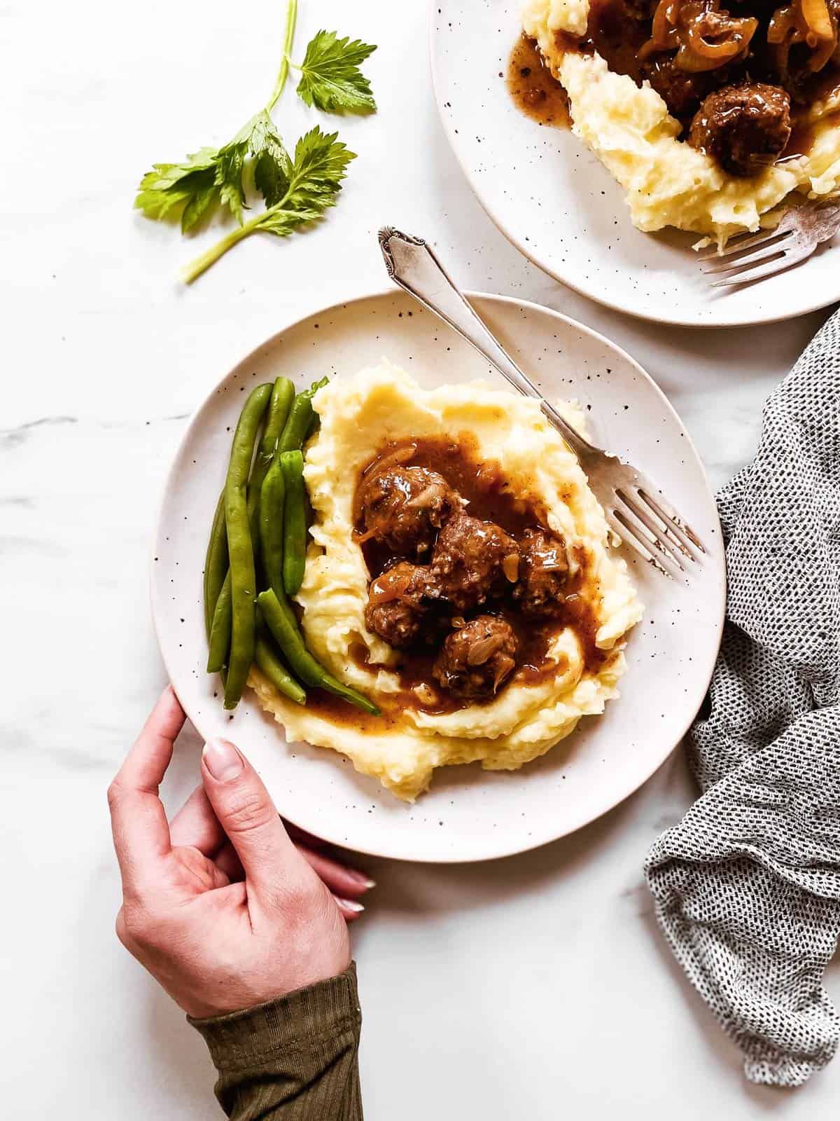 female hand holding plate with mashed potatoes, meatballs, gravy and green beans