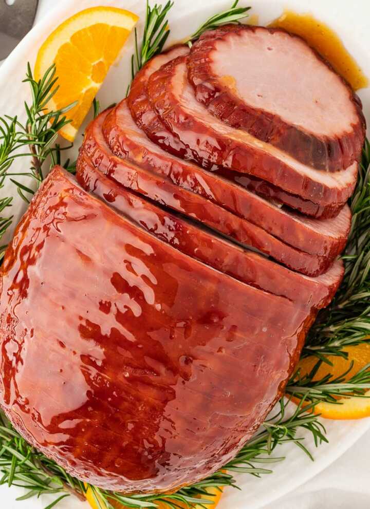 overhead view of sliced honey glazed ham on platter with rosemary and oranges