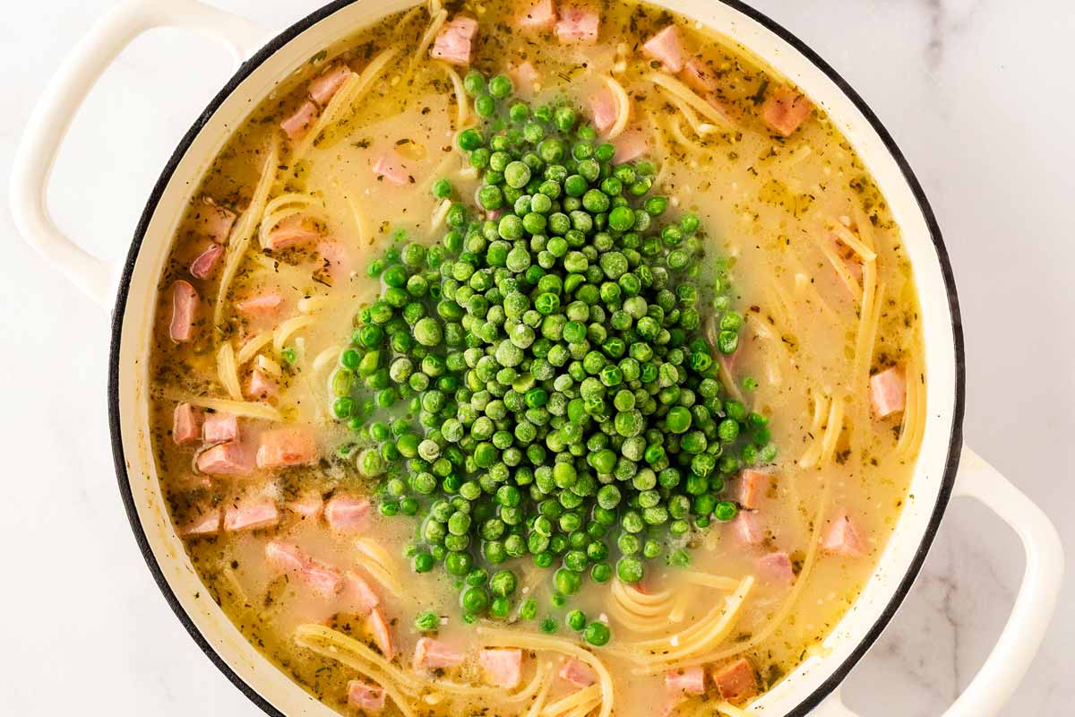 Adding peas to cooked linguine and ham.