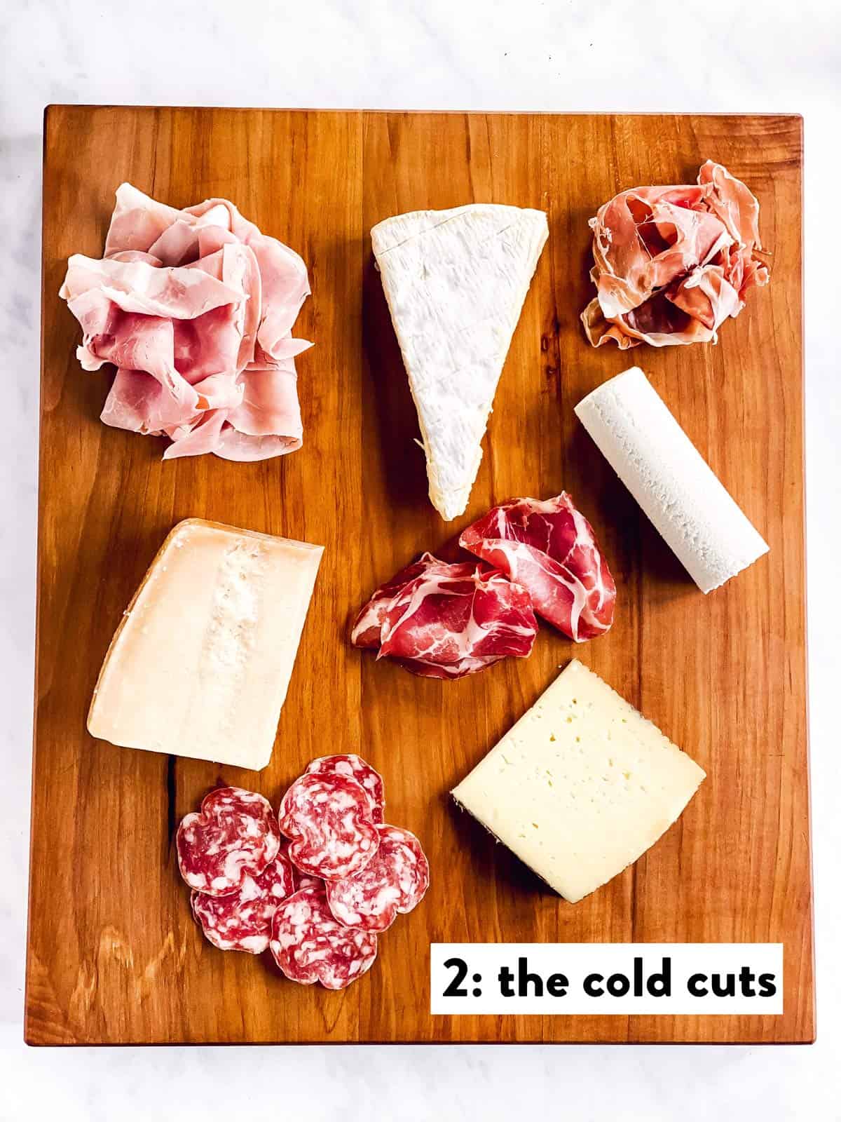 four types of cheese and cold cuts on a wooden board