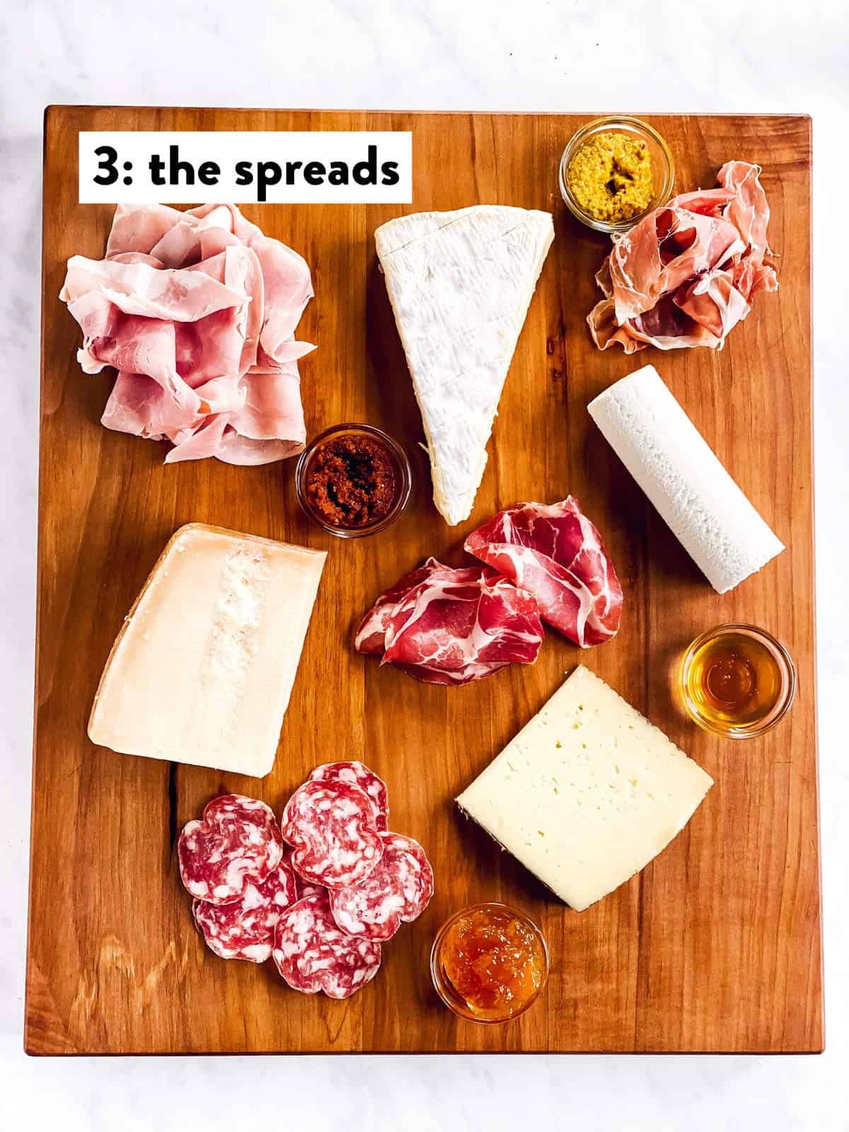 four types of cheese, cold cuts and spreads on a wooden board