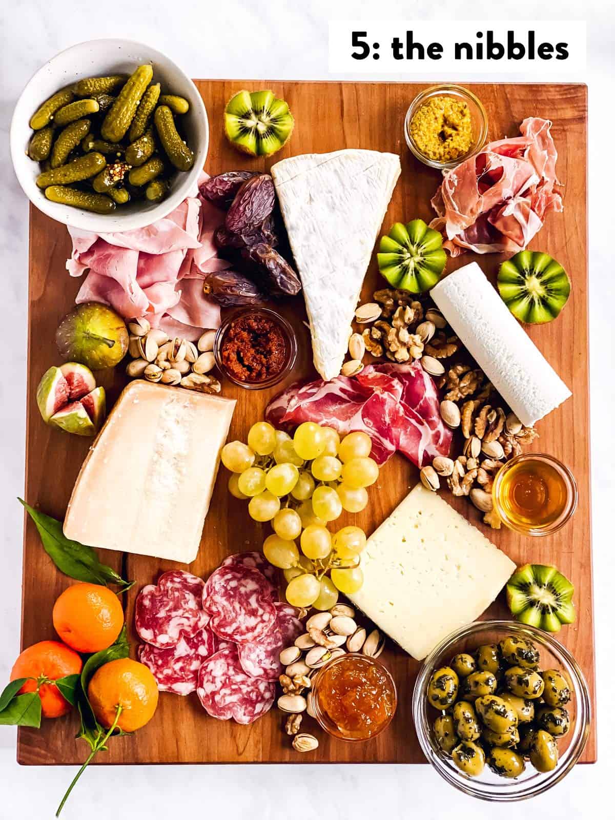 four types of cheese, cold cuts, spreads, fruit and nibbles on a wooden board