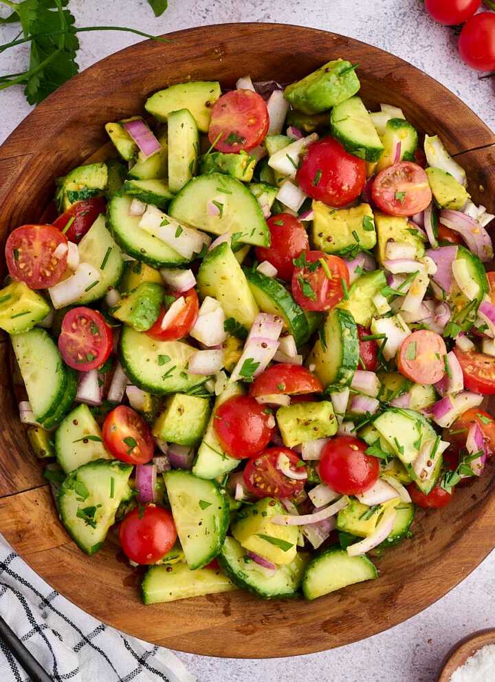 cucumber tomato avocado salad in wooden bowl