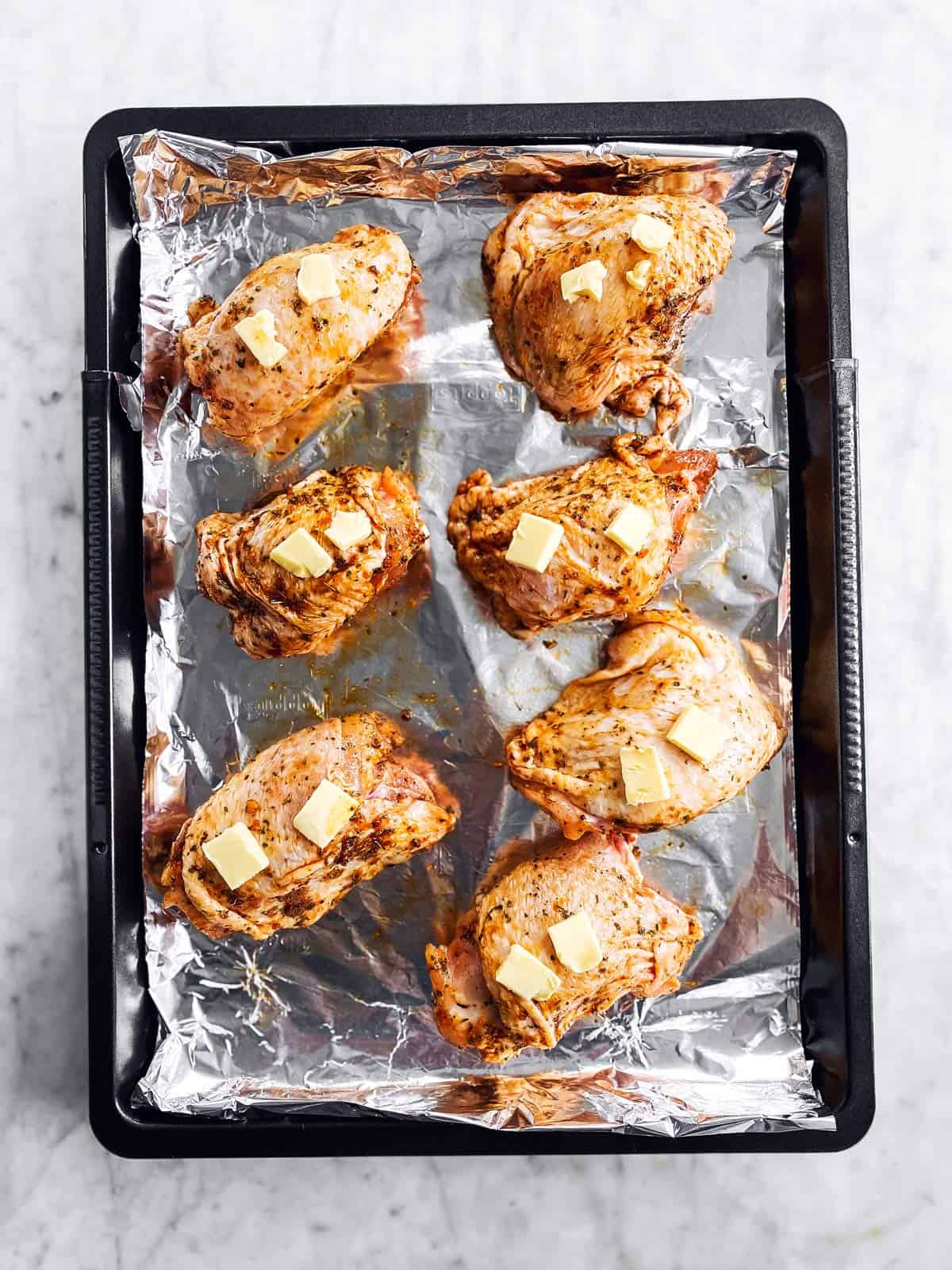 baking pan with seasoned chicken thighs dotted with butter