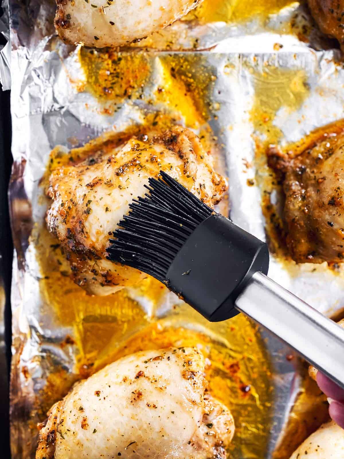 black pastry brush basting a partly cooked chicken thigh