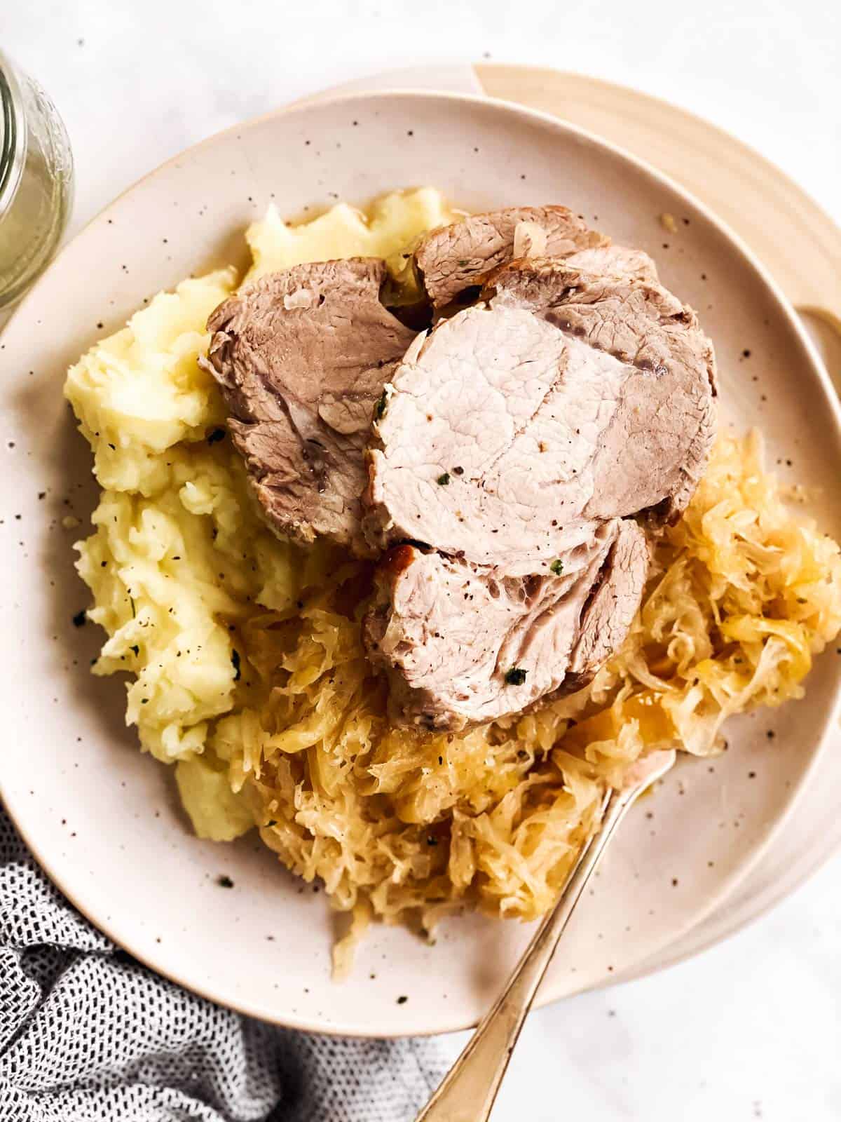 overhead view of white plate with mashed potatoes, pork roast and sauerkraut
