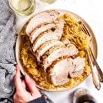 female hand holding platter with sliced pork roast and sauerkraut