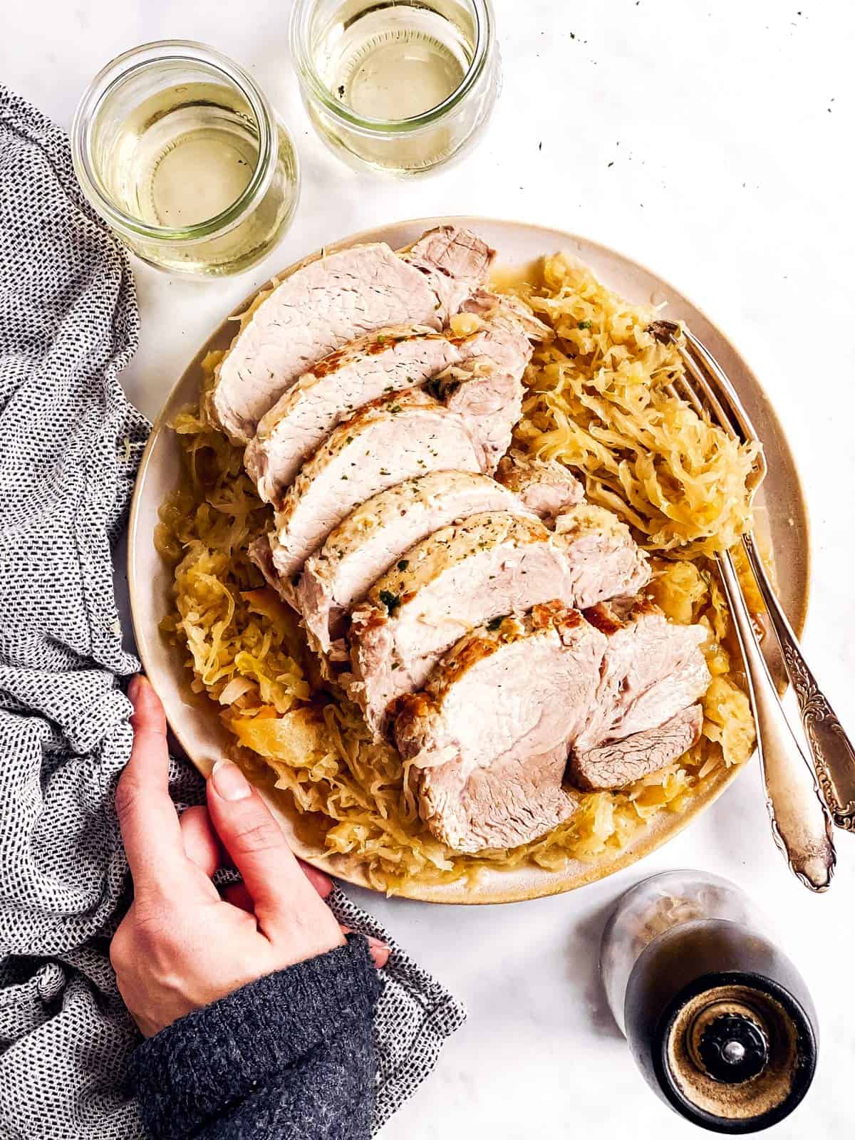 female hand holding platter with sliced pork roast and sauerkraut