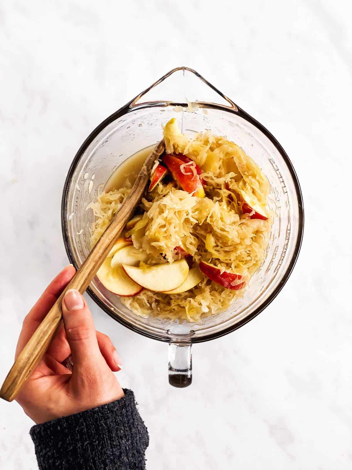 female hand stirring a bowl with sauerkraut and apples