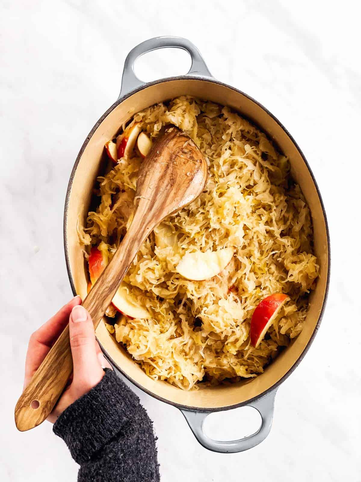 female hand smoothing out sauerkraut and apples in Dutch oven