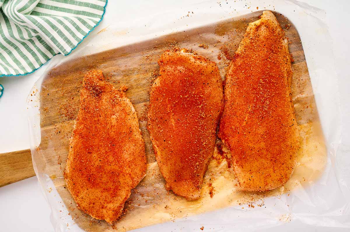 Seasoned chicken breast on a wooden board.