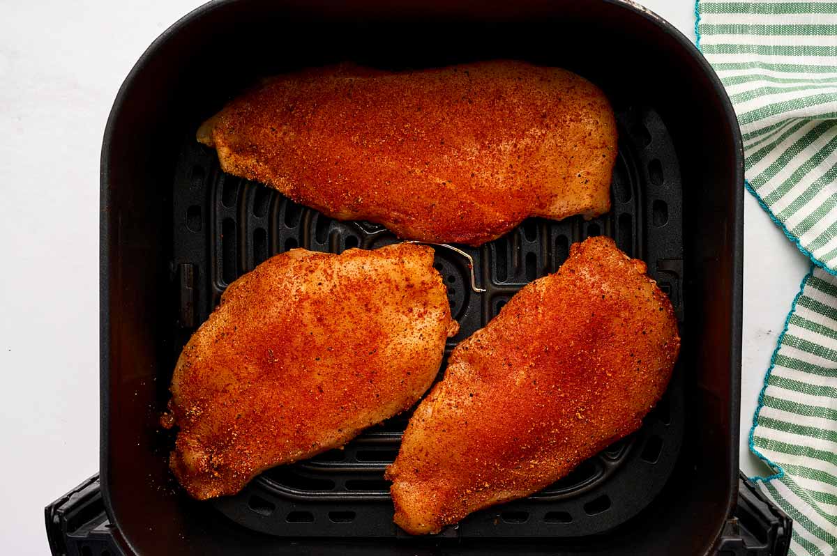 Seasoned raw chicken breast in air fryer basket.