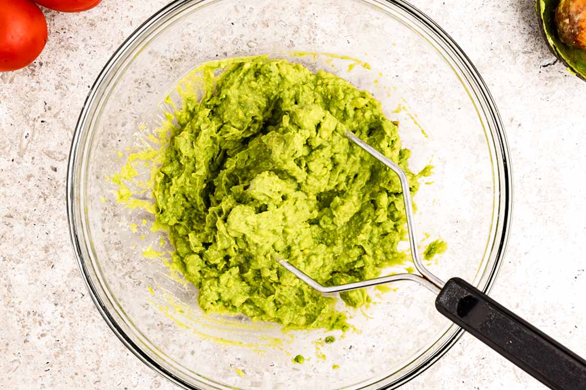Mashing avocado with a potato masher.