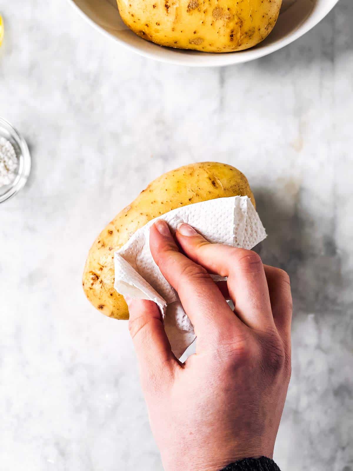 female hand drying a potato with a paper towel