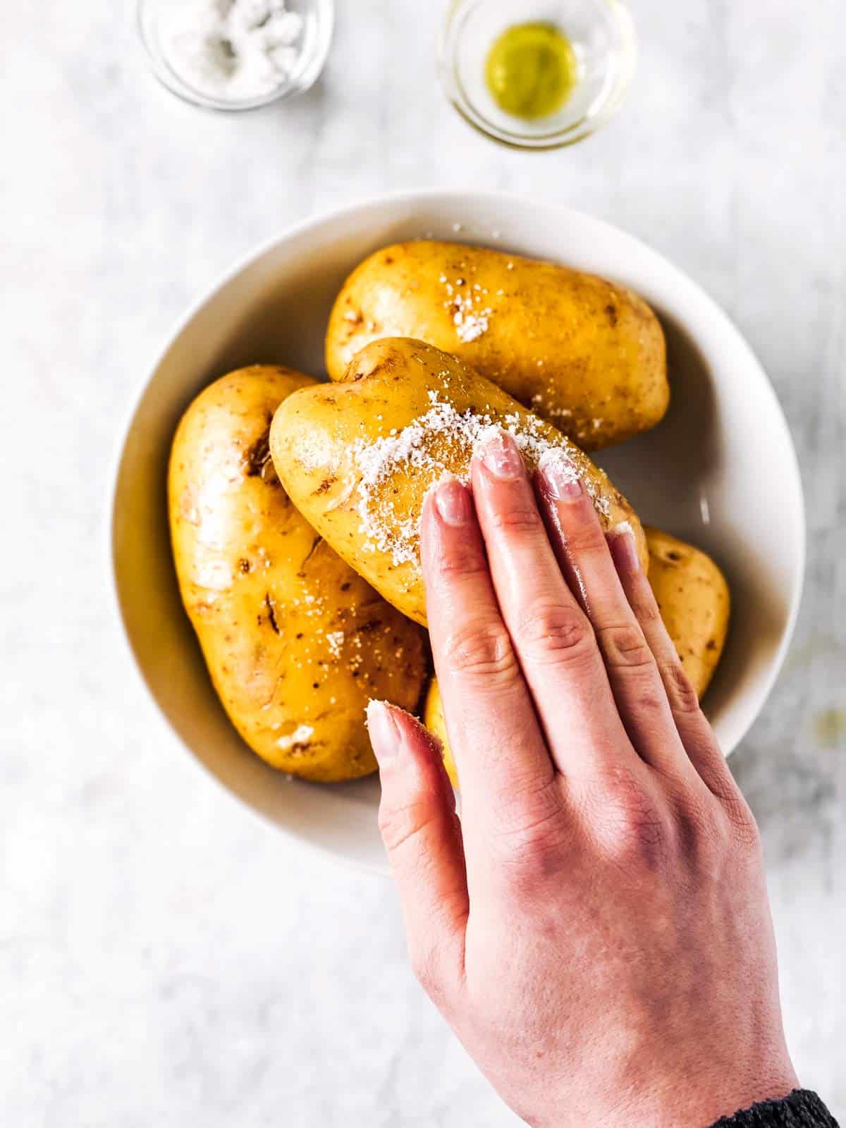 female hand rubbing salt on russet potato