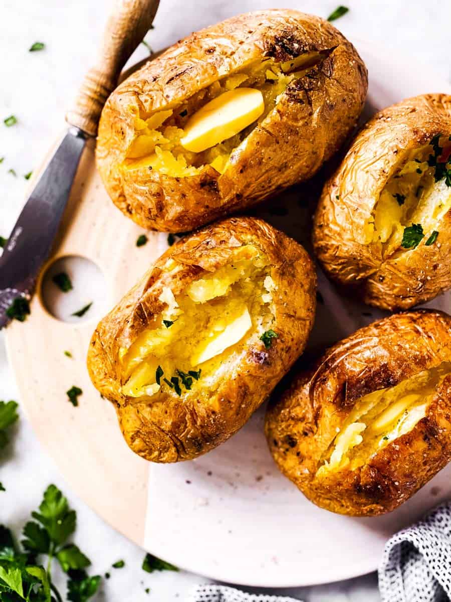 overhead view of four air fryer baked potatoes with butter and chopped parsley on serving platter