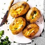 overhead view of four air fryer baked potatoes with butter and chopped parsley on serving platter