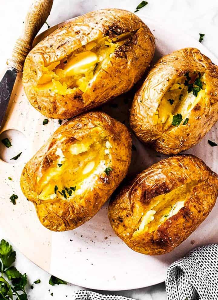 overhead view of four air fryer baked potatoes with butter and chopped parsley on serving platter