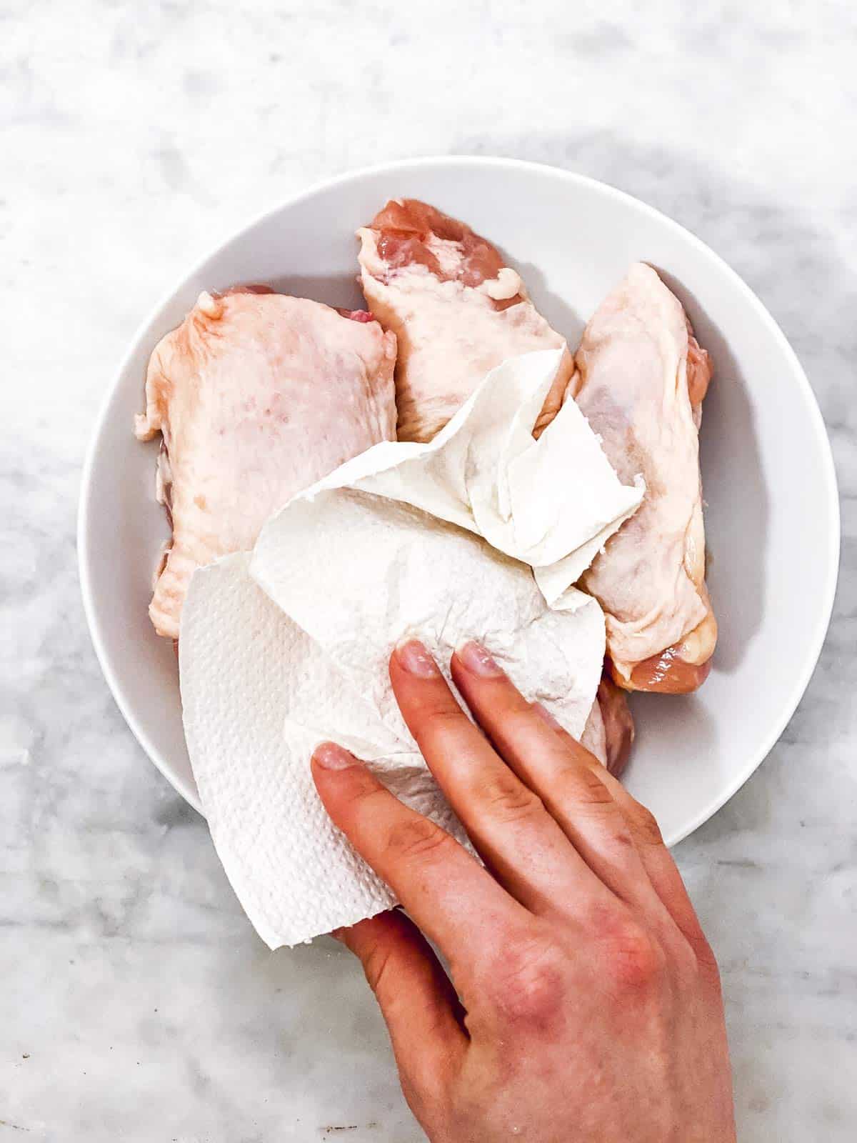 female hand patting dry chicken thighs with paper towels