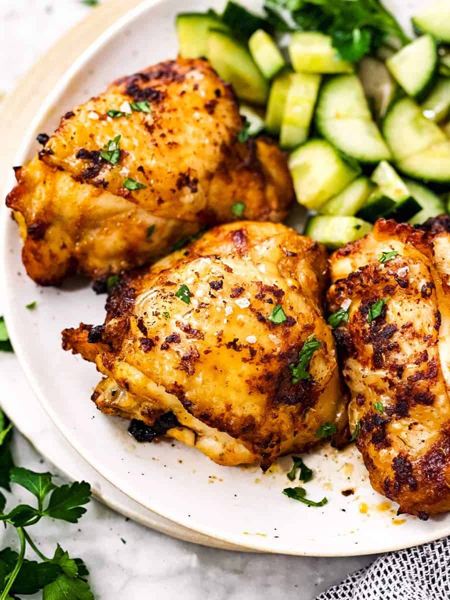 frontal view of air fried chicken thigh on white plate with cucumber salad