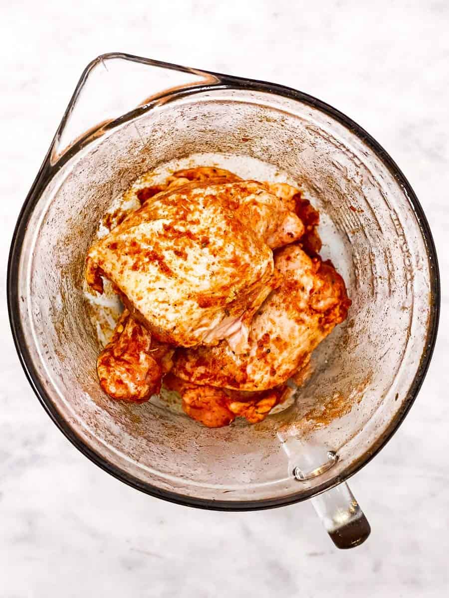 glass bowl with chicken thighs covered in seasoning