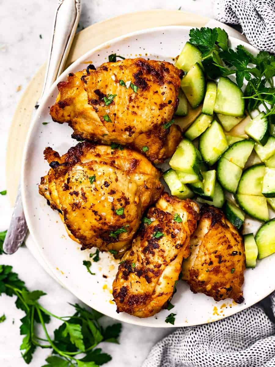 overhead view of air fryer chicken thighs on plate with cucumber