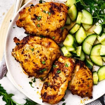 overhead view of air fryer chicken thighs on plate with cucumber