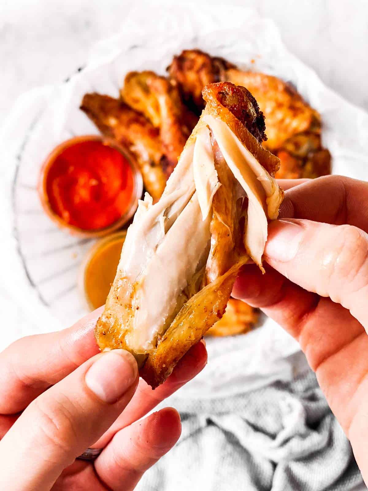 female hand pulling apart a crispy chicken wing