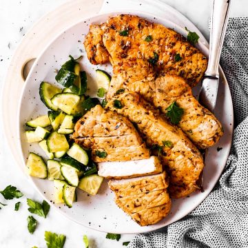 overhead view of air fried pork chops with cucumber salad on white plate