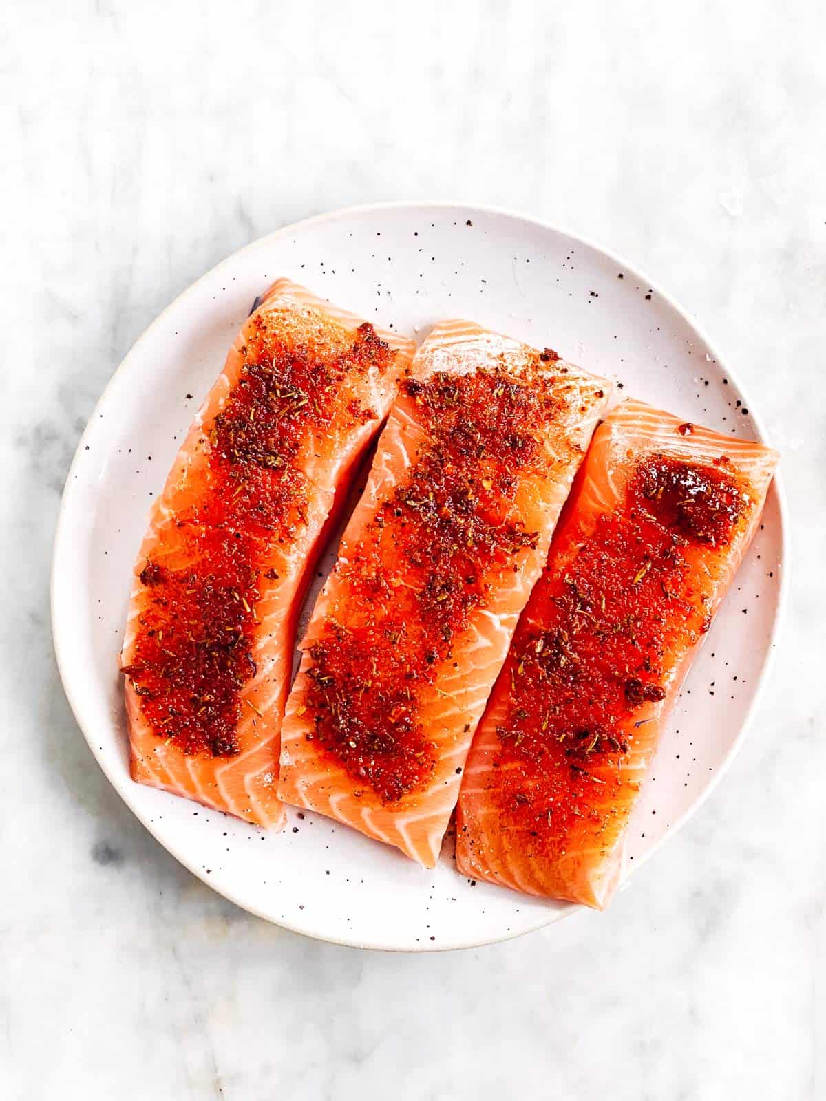 there seasoned raw salmon fillets on white plate