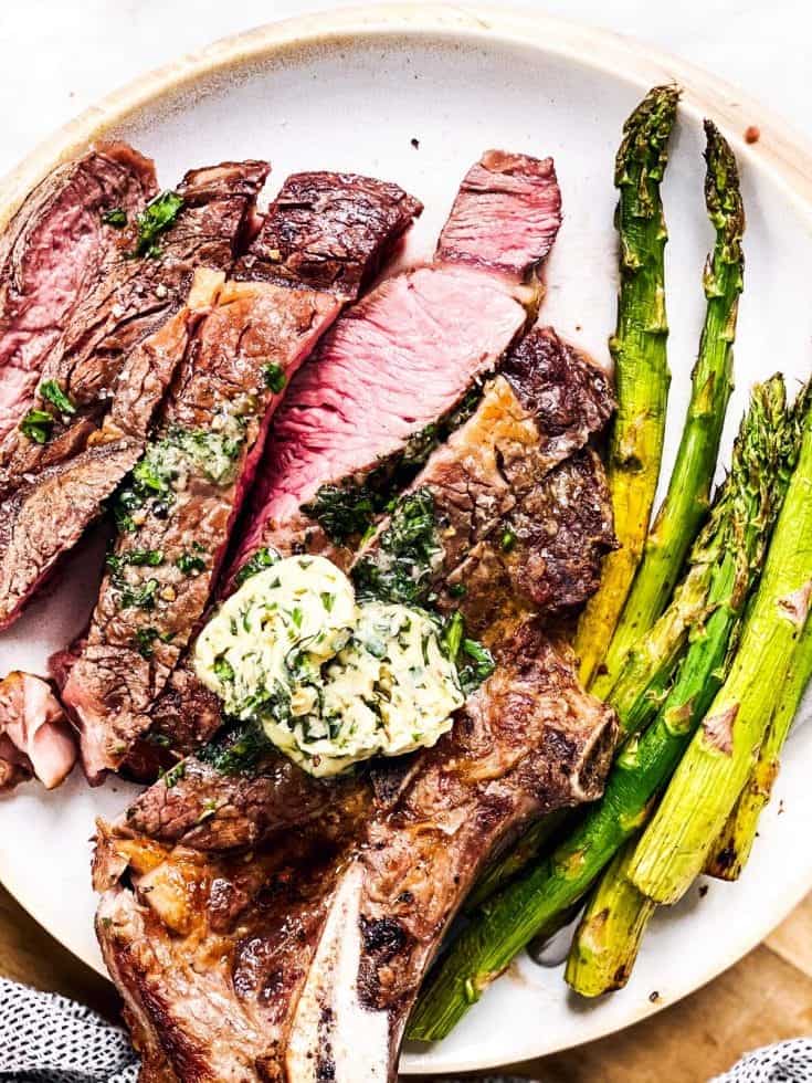 close up photo of sliced steak with garlic herb butter and asparagus on white plate