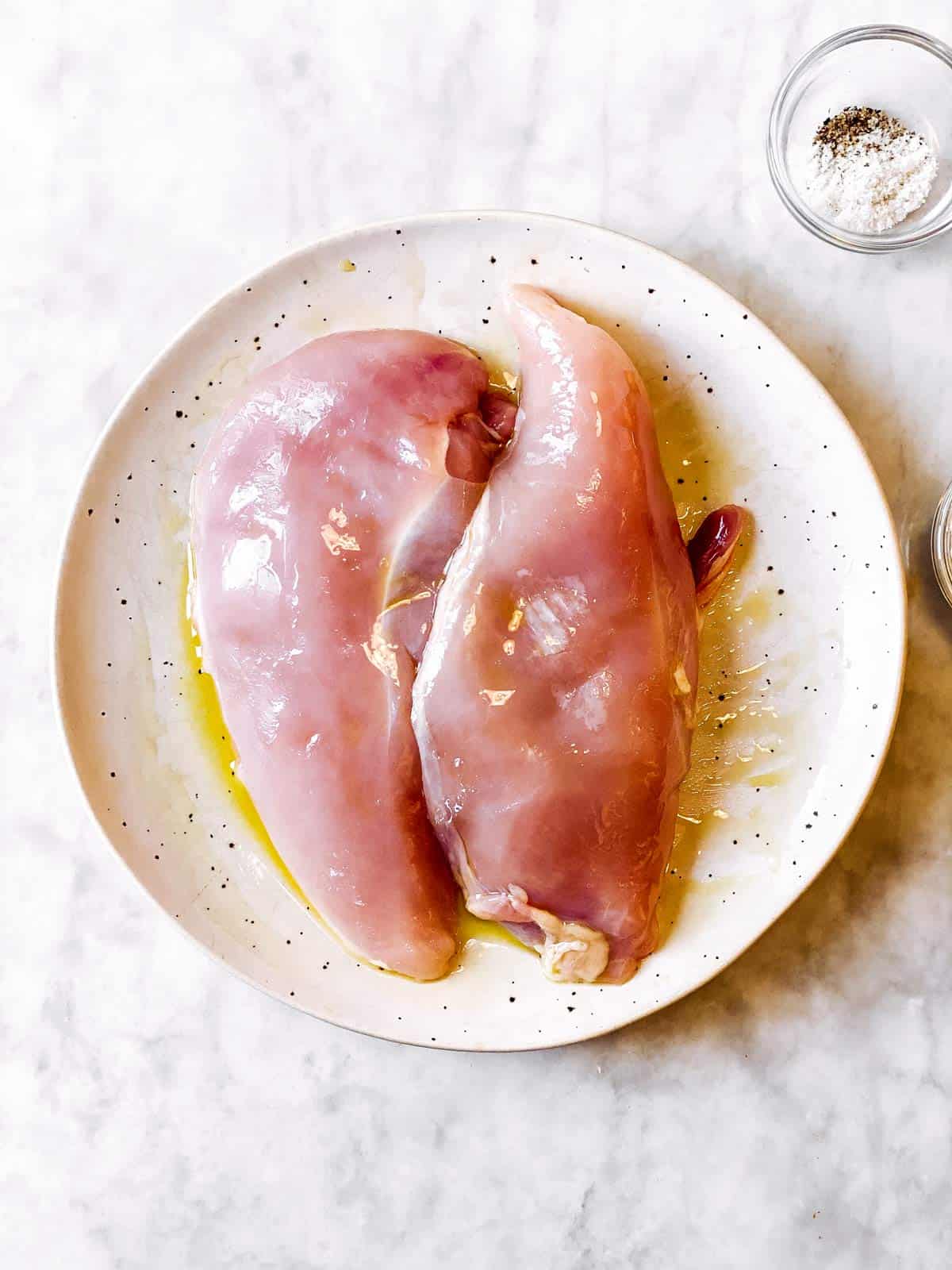 raw chicken breasts coated in olive oil on white plate