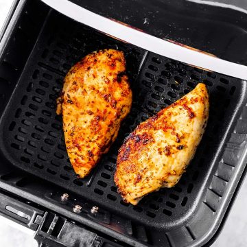 overhead view of air fryer basket with two cooked chicken breasts inside