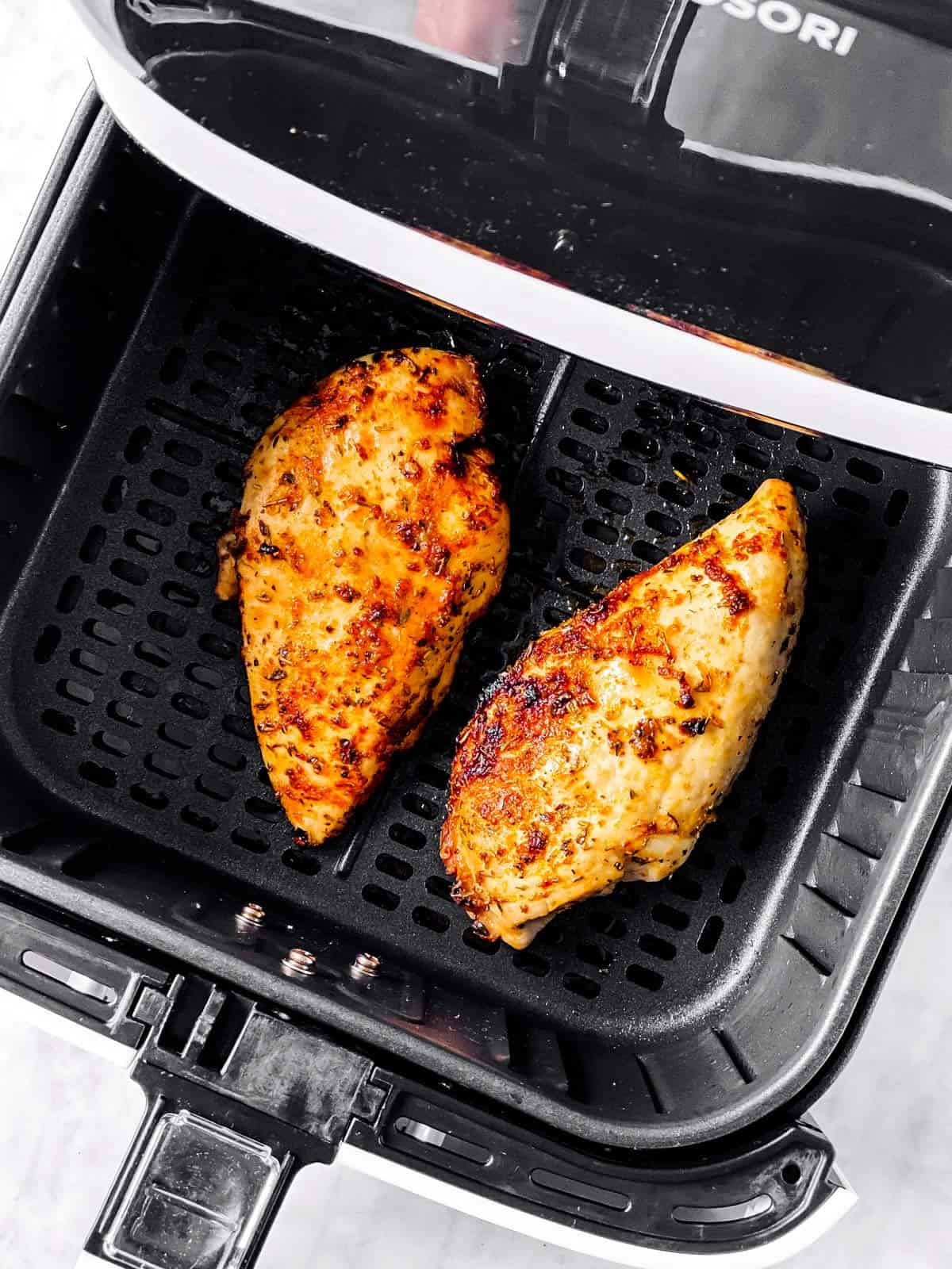 overhead view of air fryer basket with two cooked chicken breasts inside