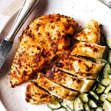 overhead view of sliced airy fryer chicken breasts on white plate with cucumber salad